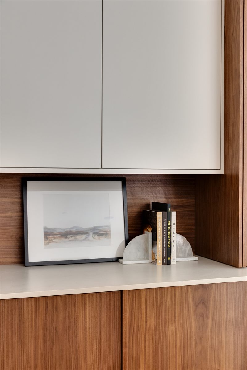Framed landscape print and marble bookends styled on a walnut credenza below white upper cabinets