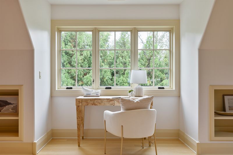 Study nook with a stone-topped desk, cream chair and a bank of windows onto the trees