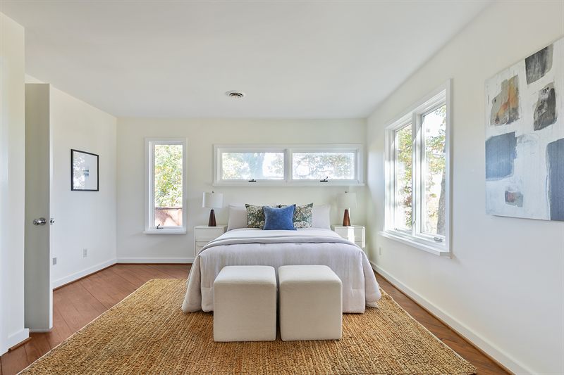Bright bedroom with a jute rug, two upholstered stools at the foot of the bed and abstract art