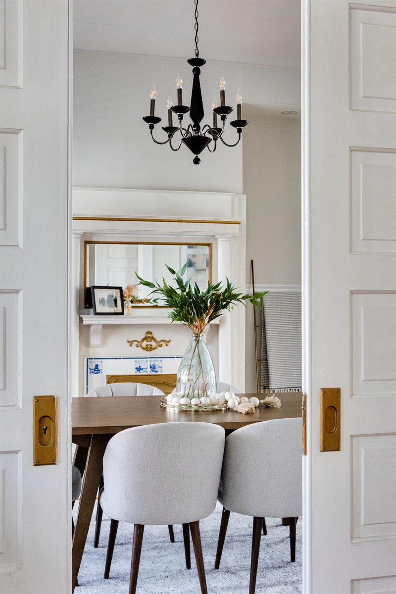 Dining room seen through open pocket doors, with a black chandelier and olive branches on the table