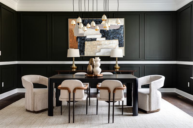 Wide view of a green panelled dining room with cream chairs, brass lamps and a large abstract canvas