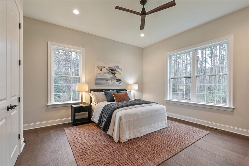 Bedroom with a ceiling fan, abstract art above the bed and a rust-toned rug over dark wood floors