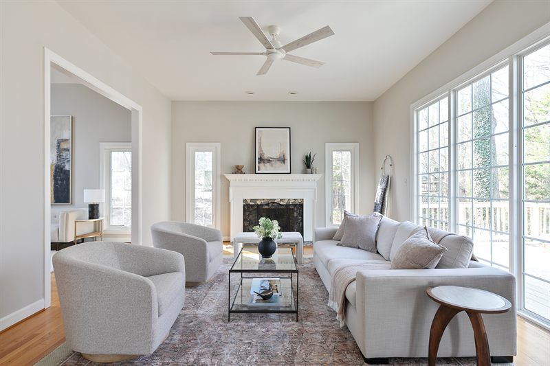 Living room with a white fireplace, grey swivel chairs and a glass coffee table by tall windows
