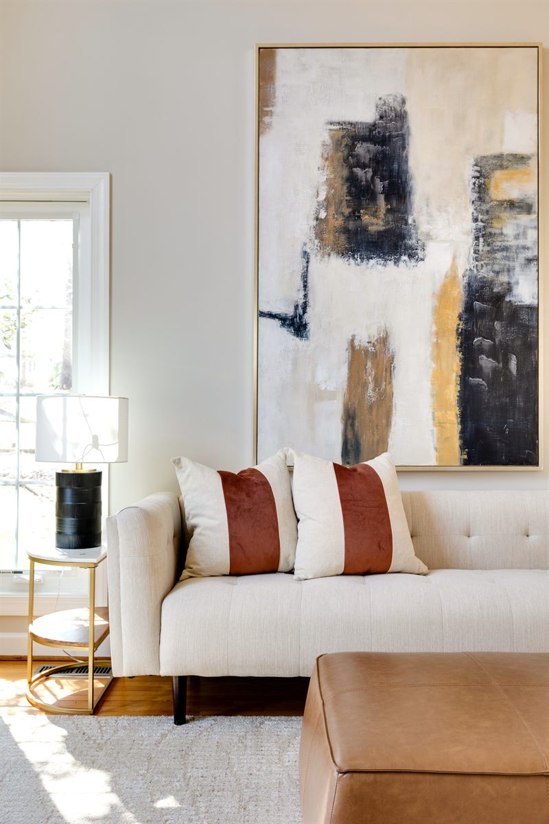Large abstract canvas above a cream sofa with rust velvet pillows and a leather ottoman