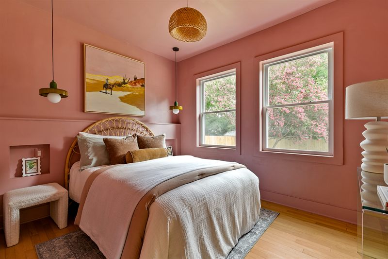 Bedroom with terracotta walls, a rattan headboard, desert landscape painting and a globe pendant