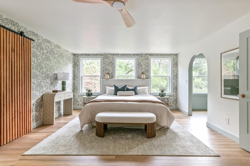 Primary bedroom with botanical wallpaper, an upholstered bed, bench and a sliding barn door