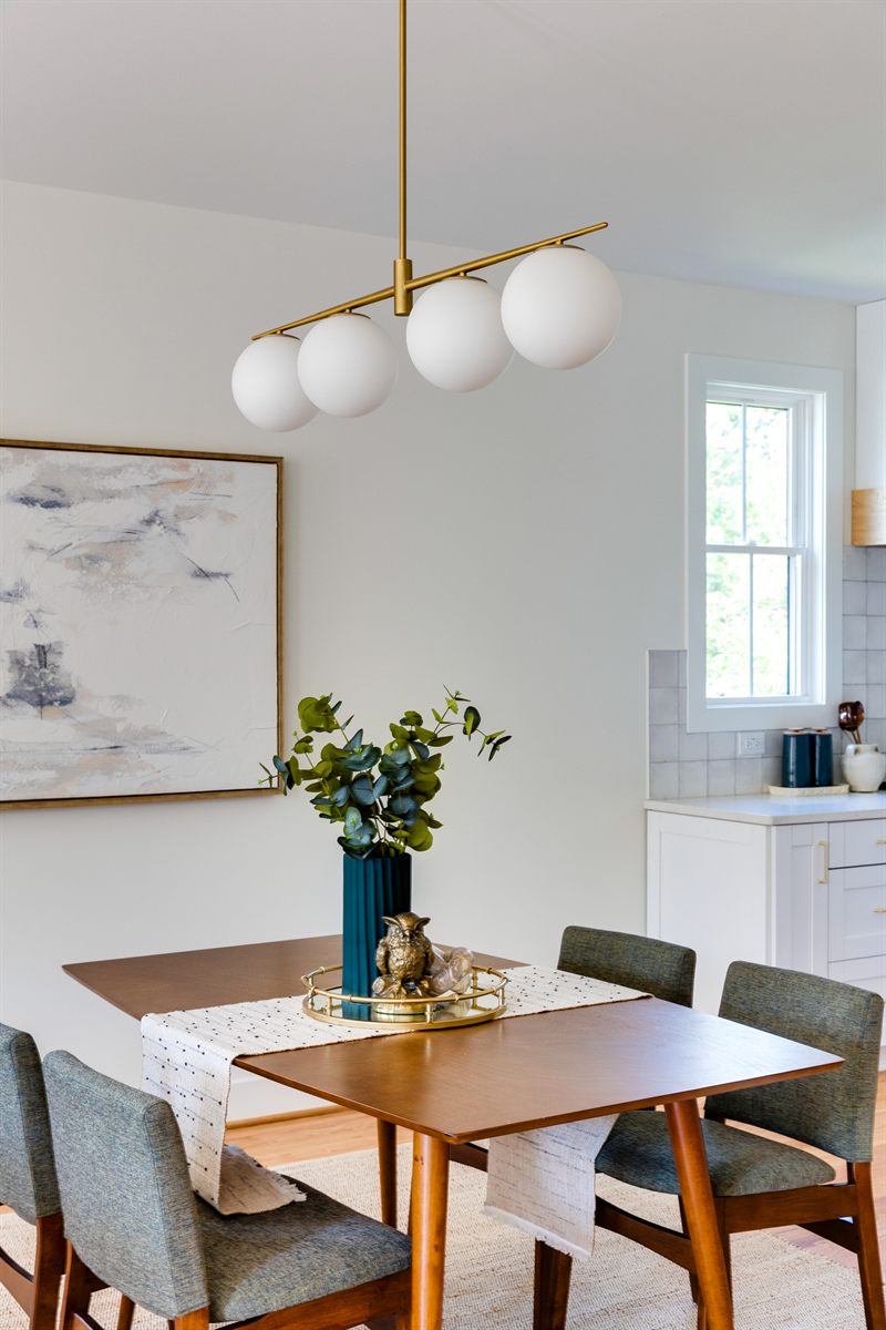 Dining table with green chairs under a brass four-globe chandelier beside a large abstract canvas